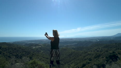 Female-runner-taking-a-break-in-the-mountains-and-making-a-video-of-the-beautiful-view