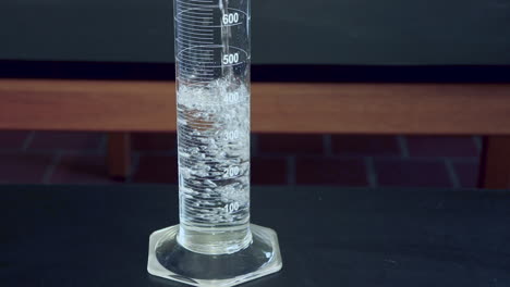 Close-up-of-Clear-liquid-being-poured-into-a-1000mL-graduated-cylinder-on-a-black-lab-bench-in-a-high-school-chimistry-classroom