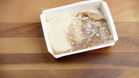 Eisgefrorenes-Essen-In-Einem-Mahlzeitboxbehälter,-Der-Auf-Einen-Hölzernen-Esstisch-Geworfen-Wird
