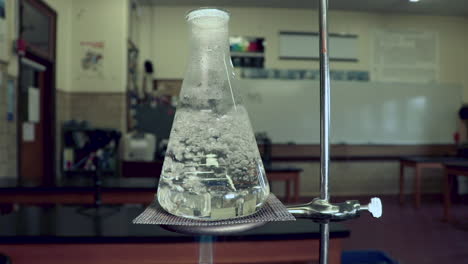 Water-boiling-in-an-erlenmeyer-flask,-heated-by-bunsen-burner-in-a-chemistry-classroom