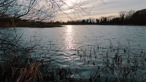 Ziehen-Sie-über-Einen-See,-Während-Sich-Der-Goldene-Sonnenuntergang-Auf-Der-Wasseroberfläche-Spiegelt