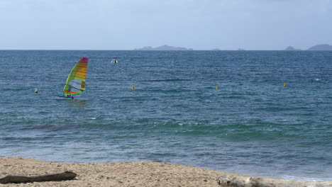 Windsurfista-Deslizándose-Por-La-Superficie-Del-Océano-Turquesa-Junto-A-La-Playa