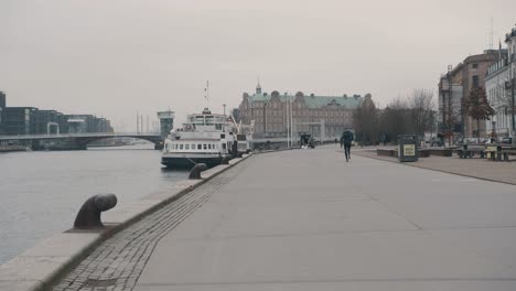 Male-jogging-on-Copenhagen-waterfront-in-urban-setting-views-of-waterfront-property-as-he-runs-into-distance