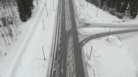 Aerial,-tilt-down,-drone-shot,-over-traffic-on-road-6,-surrounded-by-snowless-trees,-cars-turning-right-and-left-at-intersections,-on-a-cloudy,-winter-day,-in-Kontionlahti,,-North-Karelia,-Finland