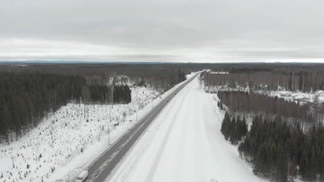 Aerial,-tracking,-drone-shot,-of-traffic,-on-road-6,-surrounded-by-snowless-trees,-on-a-cloudy,-winter-day,-in-Kontionlahti,-North-Karelia,-Finland