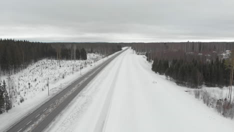 Aerial,-drone-shot,-parallel-to-road-6,-overlooking-traffic,-surrounded-by-snowless-and-leafless-trees,-on-a-cloudy,-winter-day,-in-Kontionlahti,-Pohjois-Karjala,-Finland
