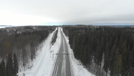 Aerial,-reverse,-drone-shot,-of-traffic,-on-road-6,-surrounded-by-snowless-trees,-on-a-cloudy,-winter-day,-in-Kontionlahti,-North-Karelia,-Finland