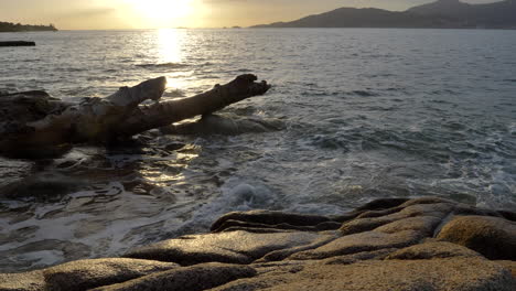 4K-Tranquil-Sunset-Ocean-Scene,-Waves-Over-Rocks-and-Driftwood