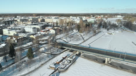 Aerial,-tracking,-drone-shot,-panning-out-from-the-cityscape,-over-traffic-on-Suvantosilta-bridge,-above-Pielisjoki-river,-on-a-sunny,-winter-day,-in-Joensuu,-Pohjois-Karjala,-Finland