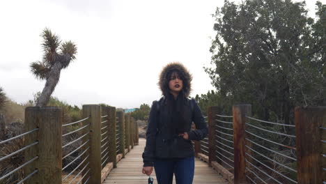 A-pretty-woman-looking-sad-and-moody-as-she-walks-a-bridge-in-the-desert-under-a-cloudy,-stormy-sky-SLOW-MOTION