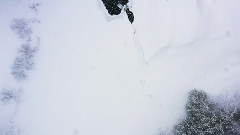 Flying-over-a-small-waterfall-on-a-frozen-river-during-a-blizzard-TOP-DOWN-AERIAL-SLOW-MOTION