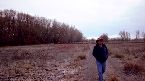Man-walks-toward-the-camera-along-a-rural-trail-on-a-cold-day