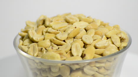 Close-up-of-salted-peanuts-in-a-glass-jar-rotating-on-a-white-background
