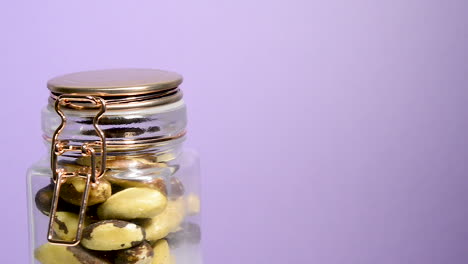 Close-up-of-an-airtight-mason-jar-rotating-with-Brazil-nuts-on-a-neon-lilac-background