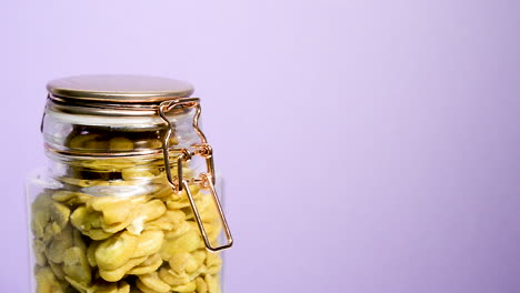 Close-up-of-an-airtight-mason-jar-rotating-with-toasted-fava-beans-on-a-neon-lilac-background