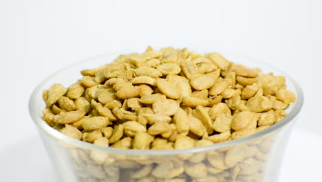 Transparent-glass-bowl-with-dry-toasted-soybeans-halves-rotating-on-a-white-background