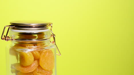 Detail-of-an-airtight-mason-jar-rotating-with-Turkish-apricot-on-a-neon-yellow-background