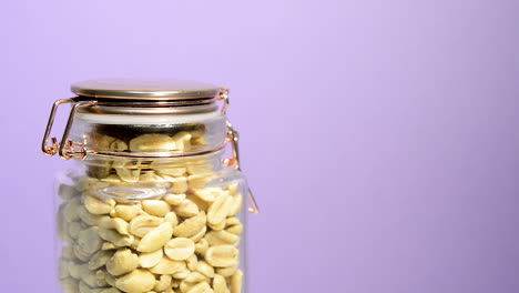 Airtight-mason-jar-rotating-with-salted-peanuts-on-a-neon-lilac-background