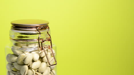 Close-up-of-an-airtight-mason-jar-rotating-with-pistachios-nuts-on-a-neon-yellow-background