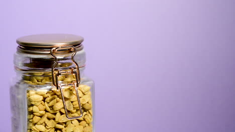 Close-up-of-an-airtight-mason-jar-rotating-with-dry-toasted-soybeans-halves-on-a-neon-lilac-background