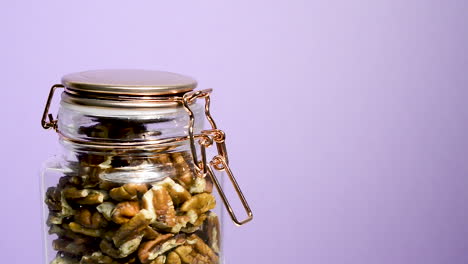 Close-up-of-an-airtight-mason-jar-rotating-with-pecan-nuts-on-a-neon-lilac-background