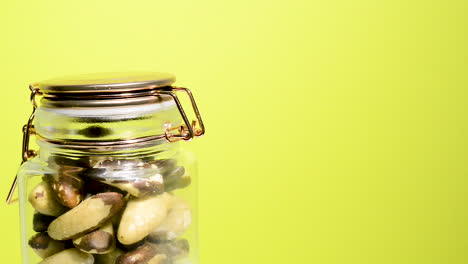 Close-up-of-an-airtight-mason-jar-rotating-with-Brazil-nuts-on-a-neon-yellow-background
