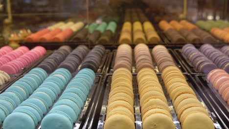 Rows-of-multicoloured-macaroons-set-out-on-display,-mirrored-reflection-in-background-as-shot-pan's-across