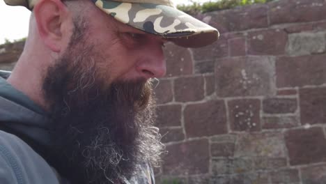 Bearded-man-wearing-baseball-cap-with-troubled-expression-walking-alongside-stone-wall