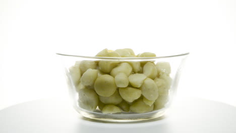 A-glass-bowl-of-macadamia-nuts-rotating-clockwise-on-a-white-background