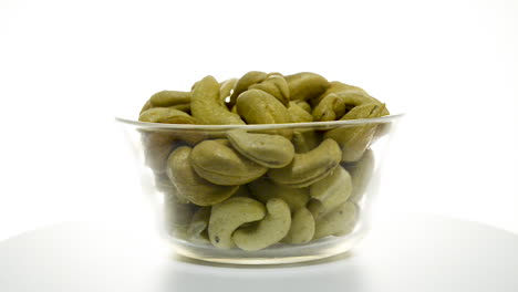 Full-glass-bowl-of-dried-cashew-nuts-rotating,-isolated-against-white-studio-background