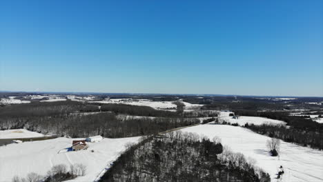 Slow-aerial-flight-over-snow-covered-farmland-under-a-clear-blue-sky