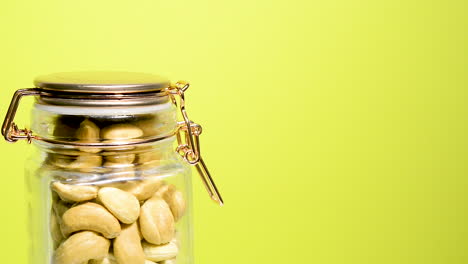 Close-up-of-an-airtight-mason-jar-rotating-with-toasted-cashew-nut-on-a-neon-yellow-background