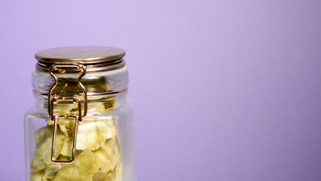 Airtight-mason-jar-rotating-with-banana-chips-on-a-neon-lilac-background