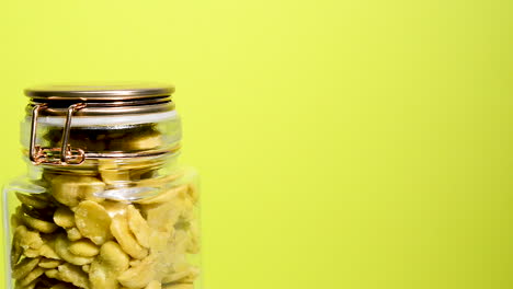 Close-up-of-an-airtight-mason-jar-rotating-with-toasted-fava-beans-on-a-neon-yellow-background