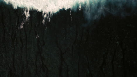Aerial-birds-eye-view-of-dramatic-dark-moody-ocean-water-with-white-foaming-waves-breaking