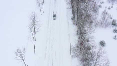 Langsam-Vorwärts-über-Eine-Schneebedeckte-Straße-Fliegen,-Während-Ein-Graues-Auto-Unter-Luftzeitlupe-Von-Oben-Nach-Unten-Fährt