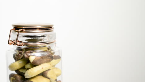 Rotating-clear-glass-clap-lock-jar-filled-with-Brazil-nuts-on-white-backdrop