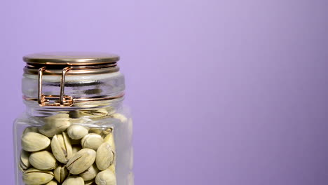 Detail-of-an-airtight-mason-jar-rotating-with-pistachios-nuts-on-a-neon-lilac-background