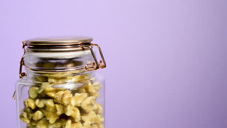 Close-up-of-an-airtight-mason-jar-rotating-with-shelled-walnuts-pieces-on-a-neon-lilac-background