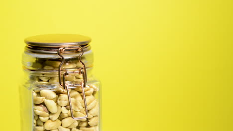 Salted-peanuts-in-an-airtight-mason-jar-rotating-on-a-neon-yellow-background
