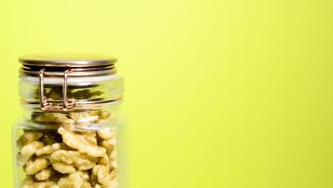 Detail-of-an-airtight-mason-jar-rotating-with-shelled-walnuts-pieces-on-a-neon-yellow-background