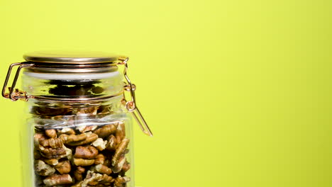 Detail-of-an-airtight-mason-jar-rotating-with-pecan-nuts-on-a-neon-yellow-background