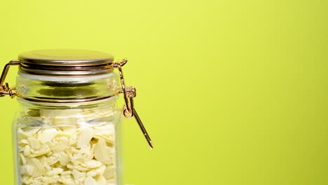 Detail-of-an-airtight-mason-jar-rotating-with-sliced-almonds-on-a-neon-yellow-background