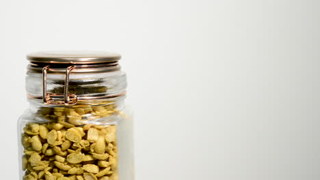 Glass-Mason-jar-full-of-raw-golden-soya-beans-rotating-set-against-white-studio-background