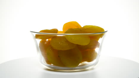 Glass-bowl-full-of-Turkish-apricots-rotating-isolated-against-white-backdrop