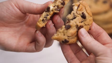 Tearing-a-warm-chocolate-chip-cookie,-gooey-chocolate-chips-pulling-apart-with-two-hands-close-up-slow-motion-4k