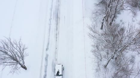 Fliegen-Sie-Rückwärts-über-Einem-Schneebedeckten-Geländewagen,-Der-Während-Eines-Blizzards-Von-Oben-Nach-Unten-Eine-Straße-Hinunterfährt