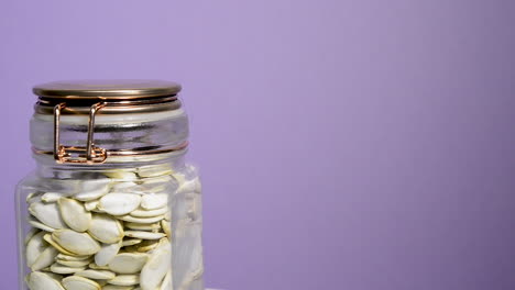 Close-up-of-an-airtight-mason-jar-rotating-with-pumpkin-seeds-on-a-neon-lilac-background