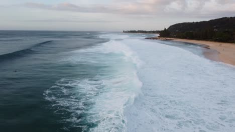 Cinematic-drone-shot-of-the-famous-waves-crashing-on-the-beach-at-Banzai-Pipeline-on-Oahu's-North-Shore-during-sunset