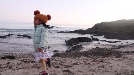 A-little-girl-in-a-beani-dances-on-a-cold-coastal-beach